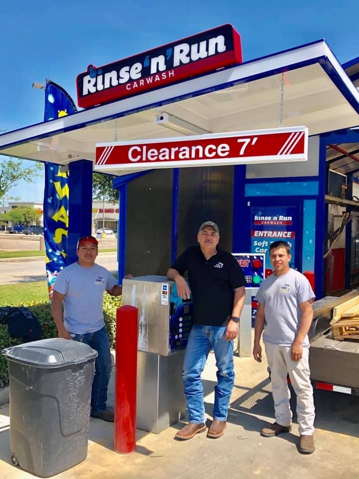Three men stand in front of a car wash with a 