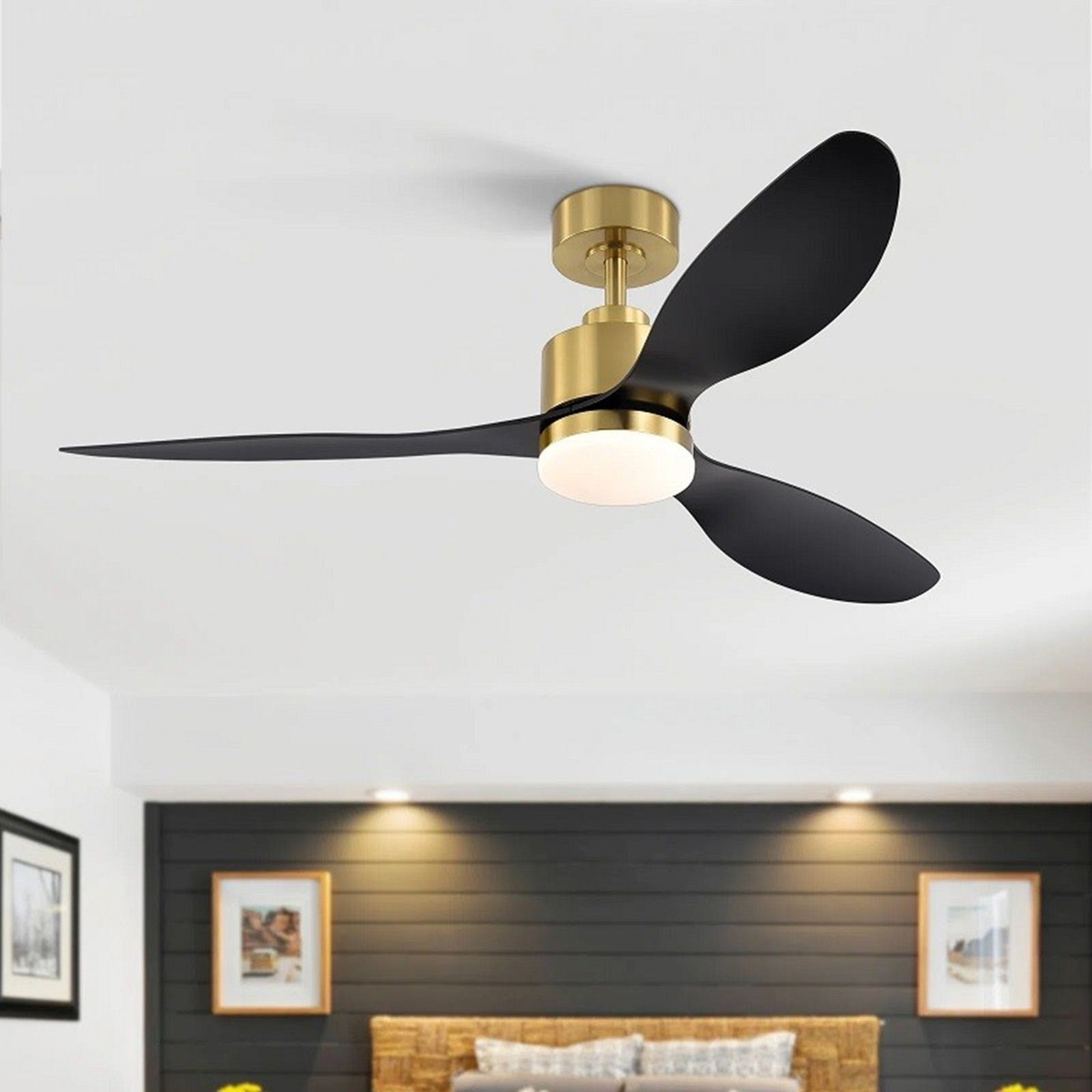 Modern three-blade ceiling fan with matte black blades and a brass finish, featuring a central light, in a bedroom.