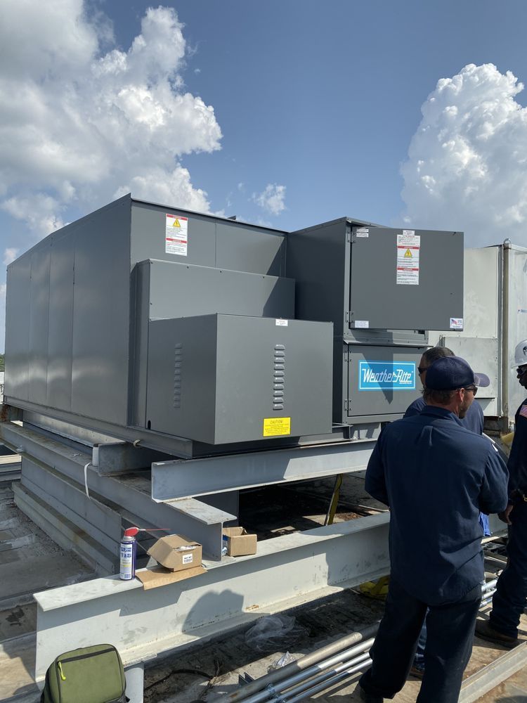 Gray rooftop HVAC unit with workers, blue sky.
