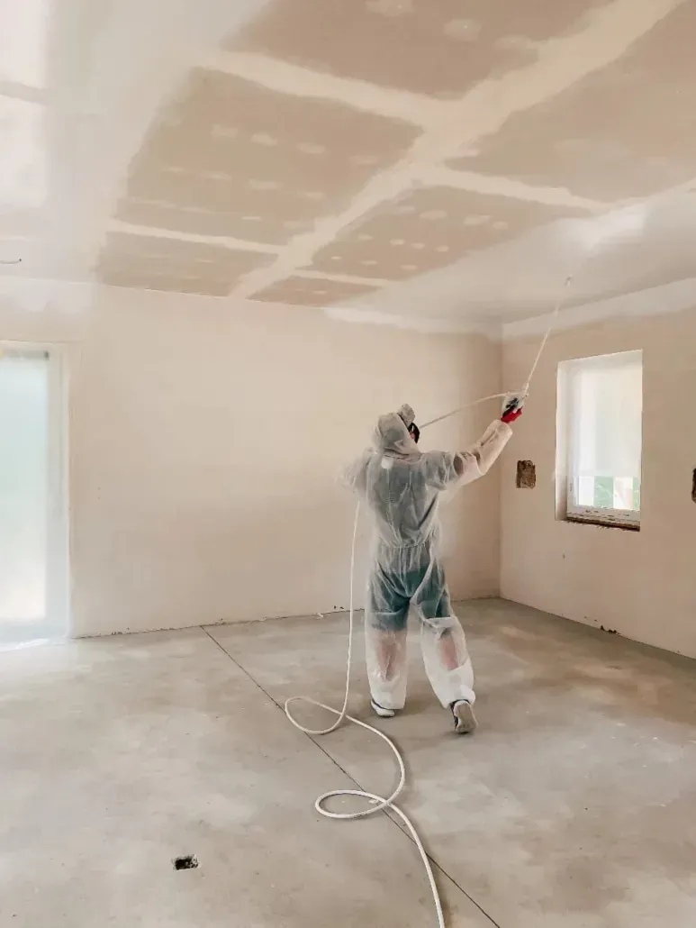 Person spraying paint on a room ceiling during interior renovation