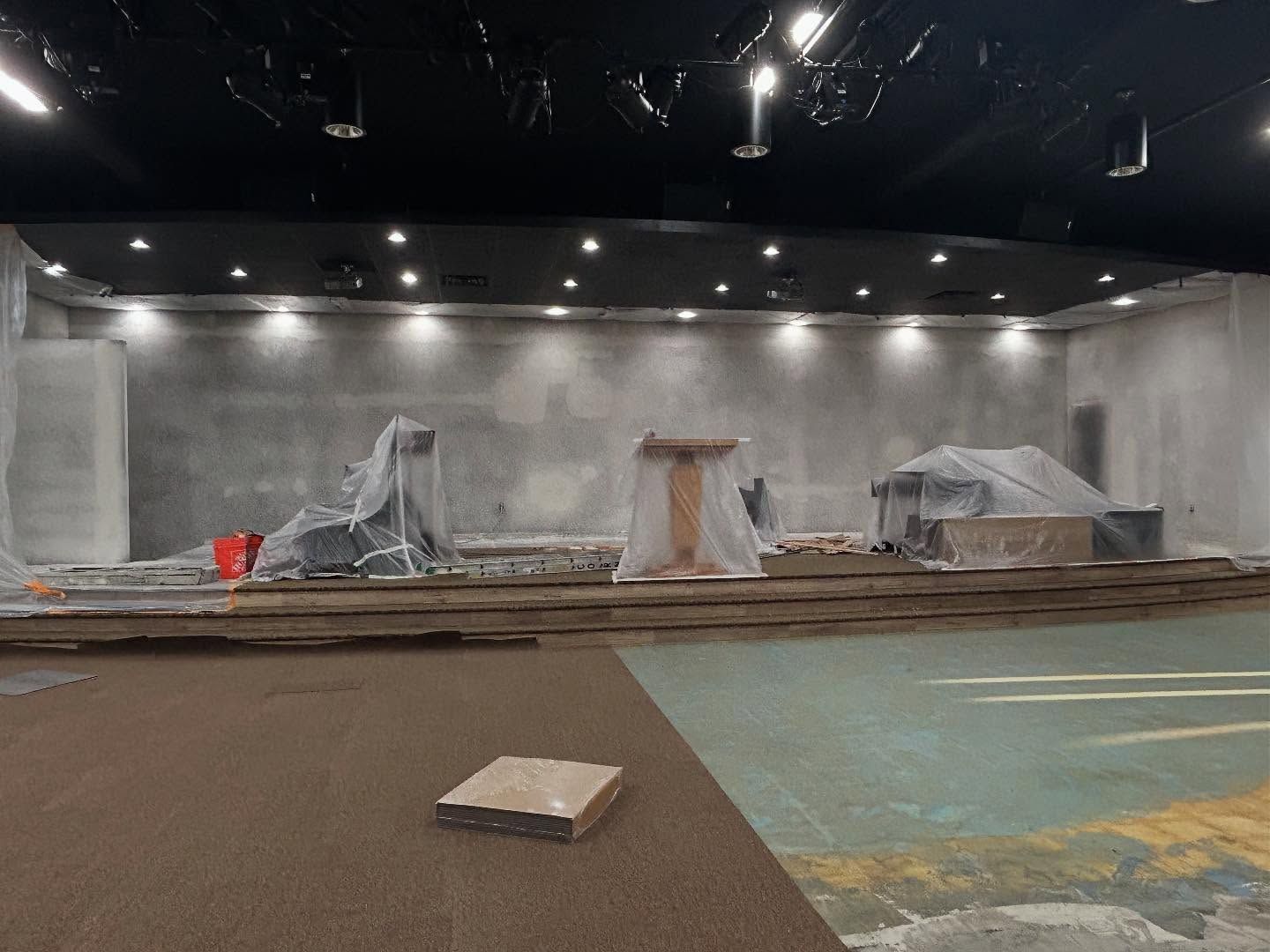 Construction site: interior of a building with covered equipment, concrete walls, and brown flooring.