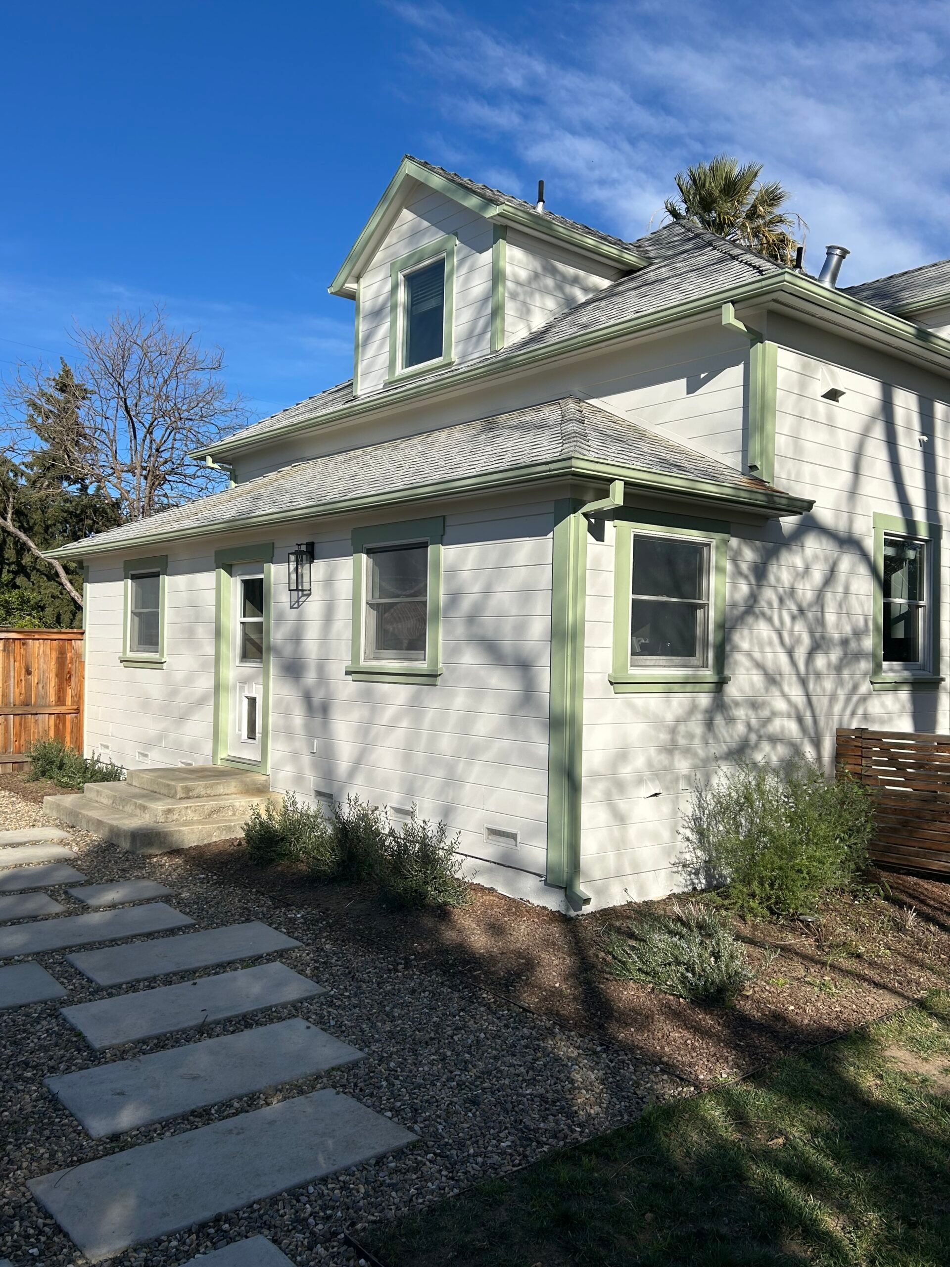 Two-story white house with green trim and tile roof, sitting under a bright blue sky.