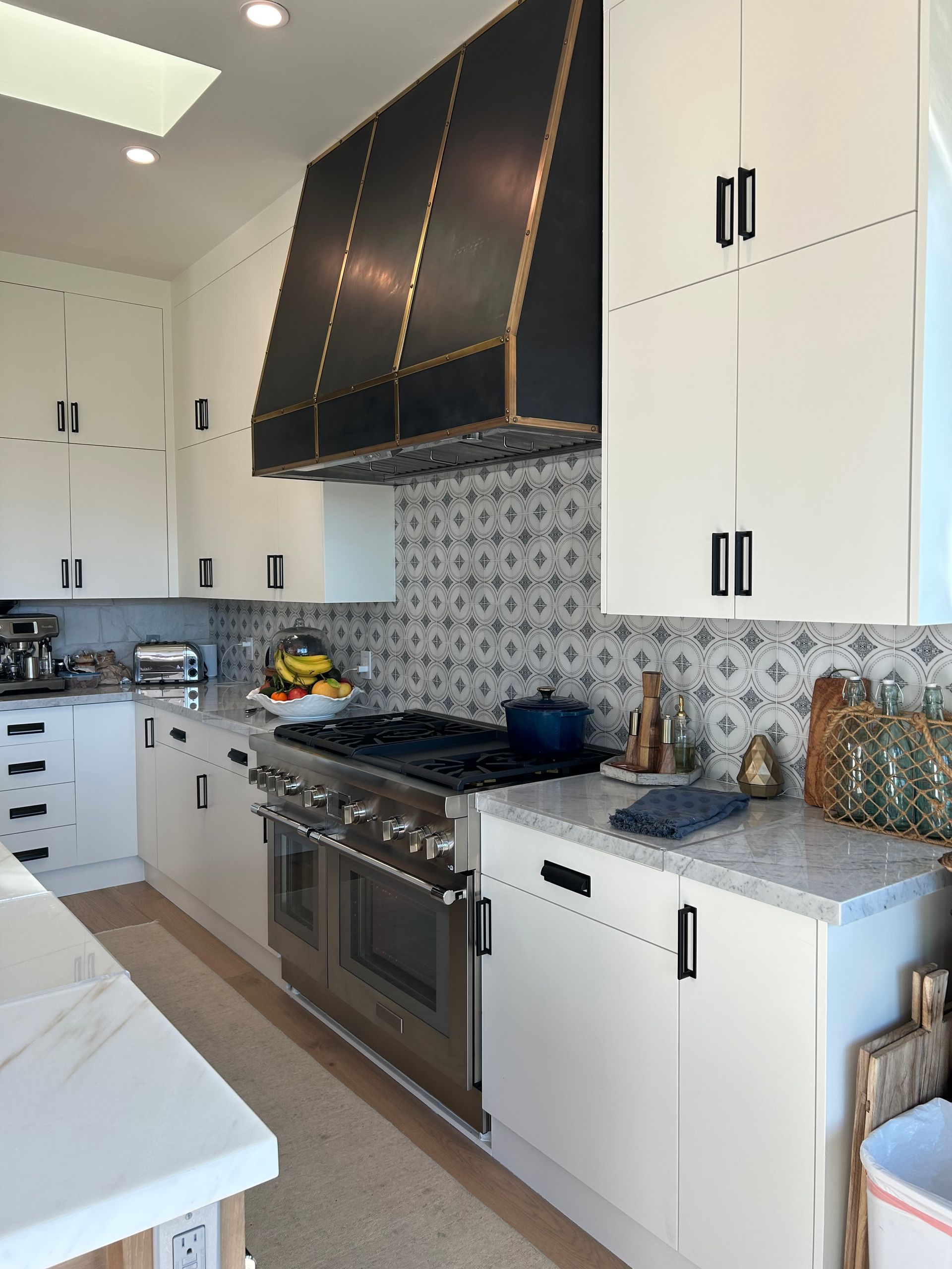 Modern white kitchen with black range hood and patterned backsplash.