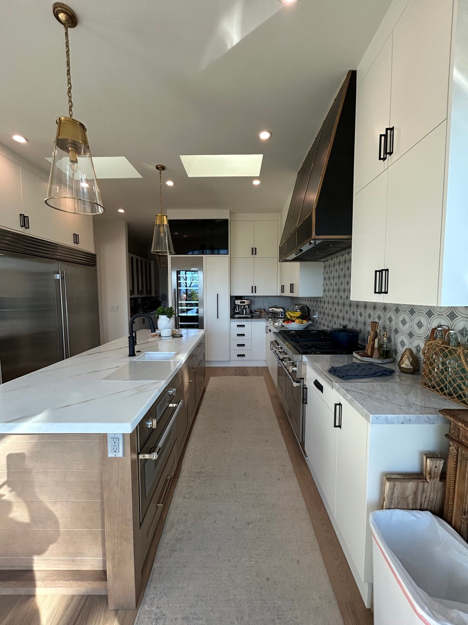 A long modern kitchen with white cabinets, light counters, a stove, and an island.