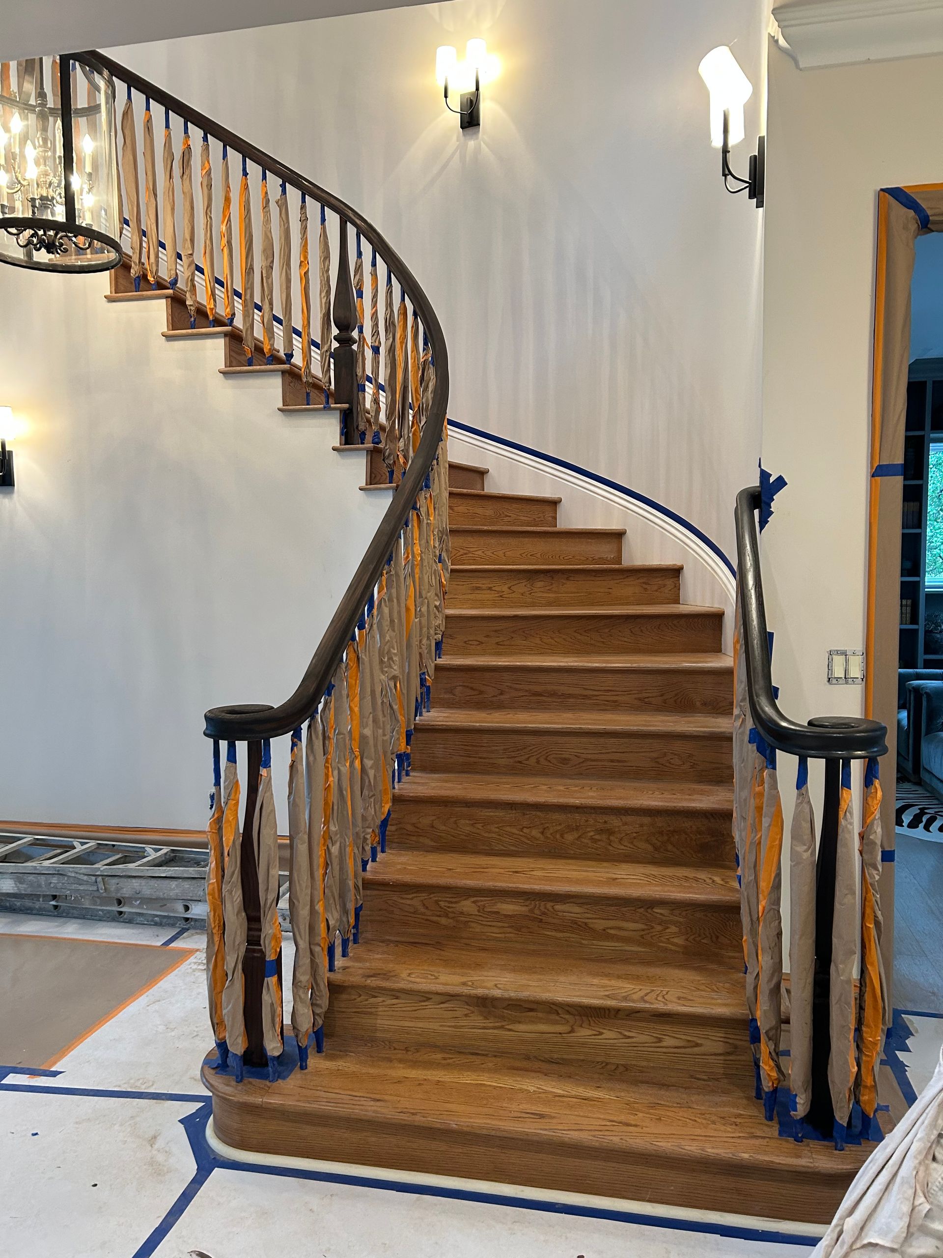 Curved wooden staircase with dark railing, light steps, and white walls.