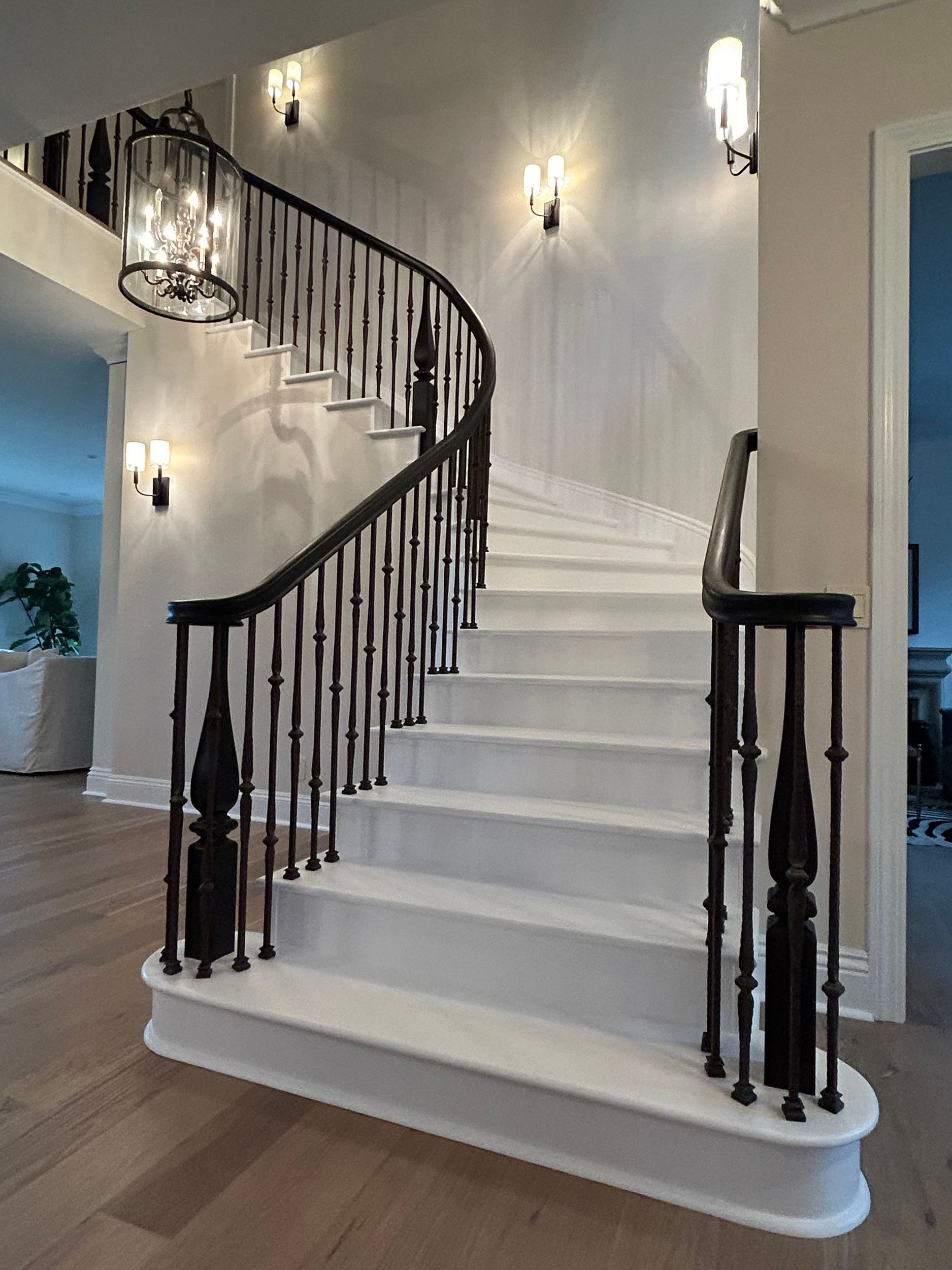Elegant, curved staircase with dark wood railing and white steps; sconces on the wall.