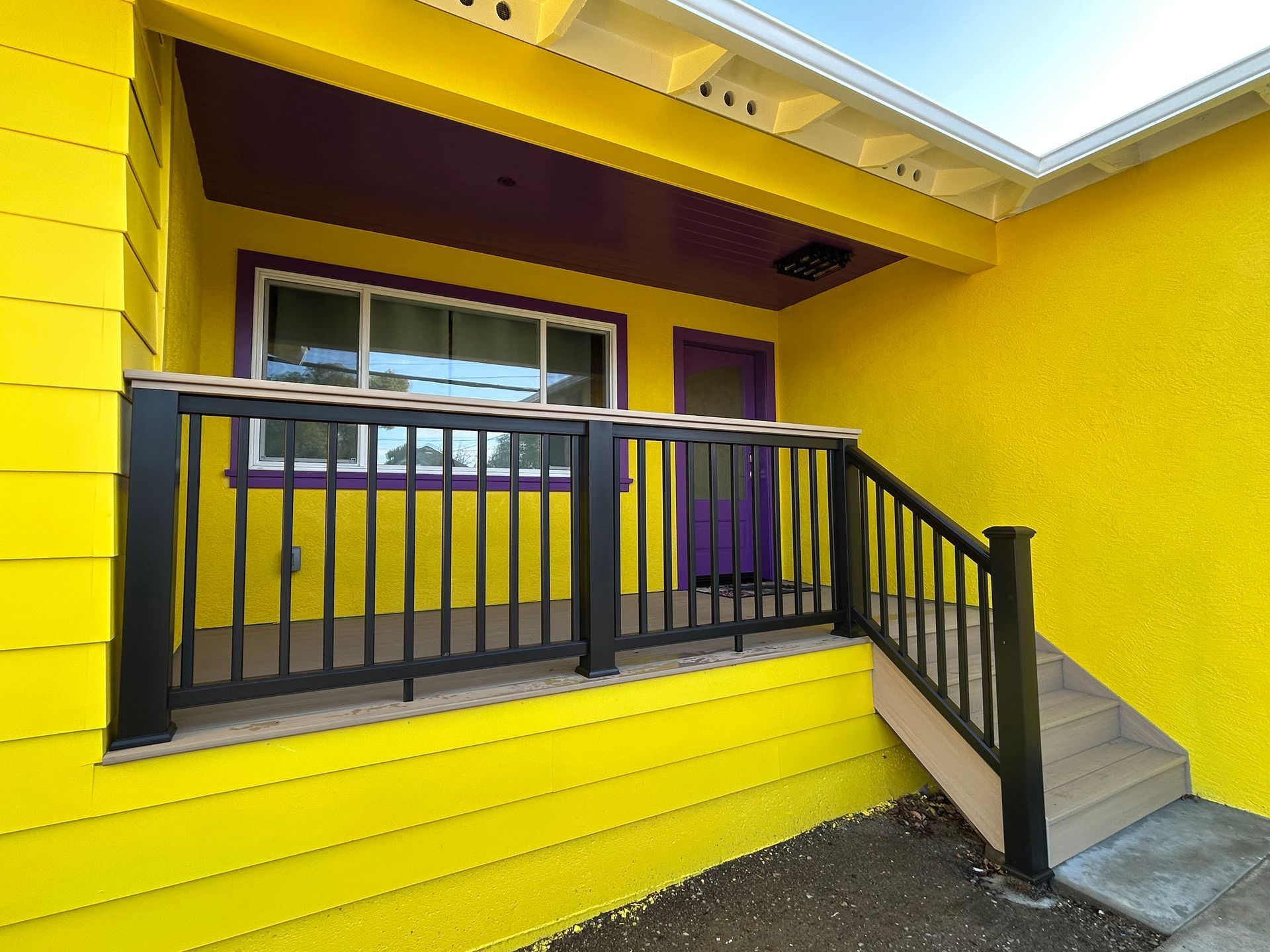 Yellow house with purple accents, black railing.