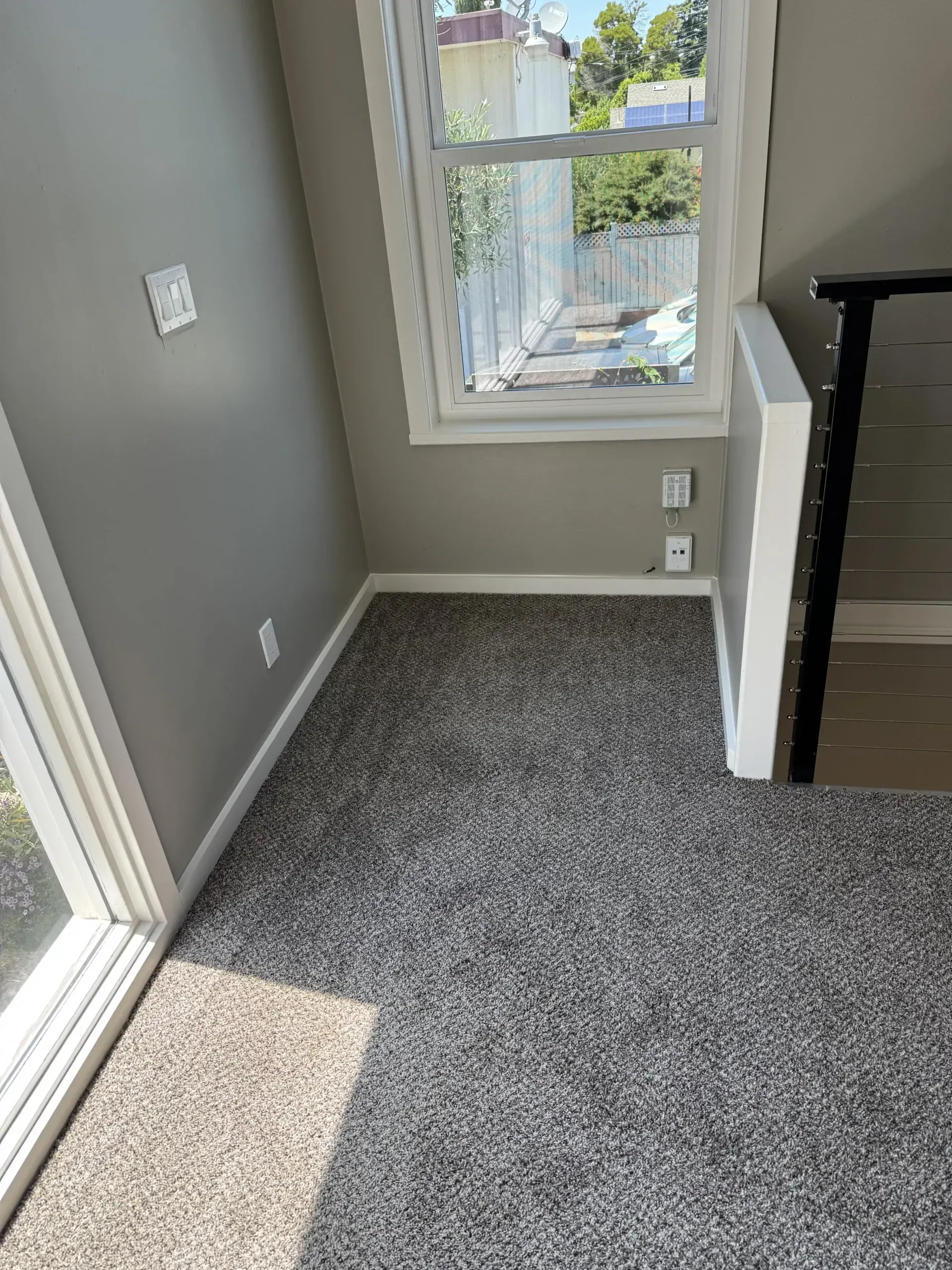 Small gray carpeted room with a window and neutral colored walls.