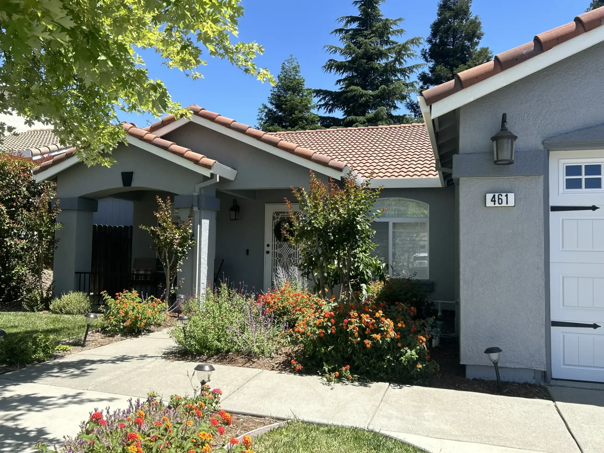 Tan house with red-tile roof, flowers, and walkway; sunny day. Number 241 on garage.