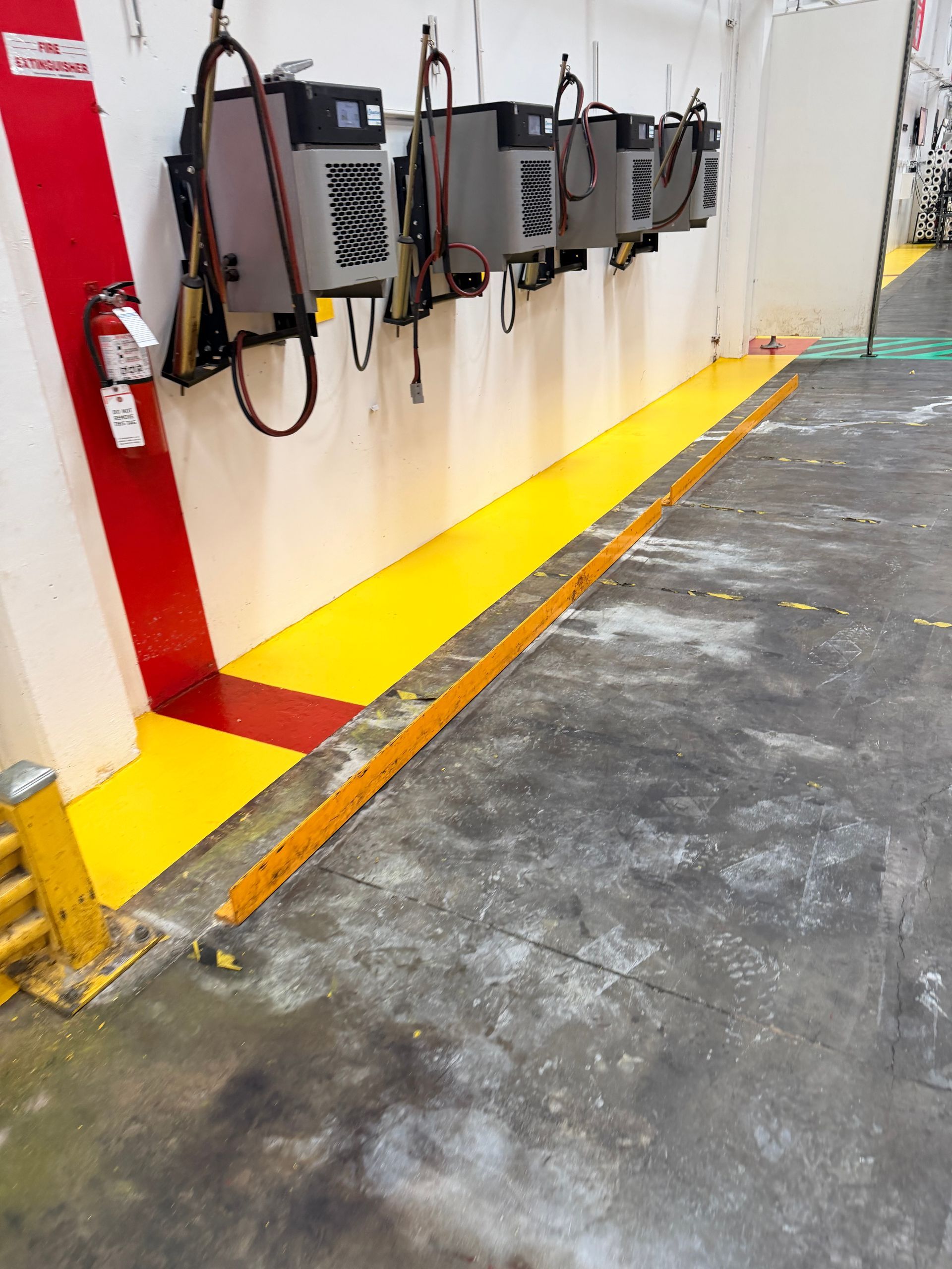 Row of gray machines hanging on a white wall, with yellow painted floor markings, and a fire extinguisher.