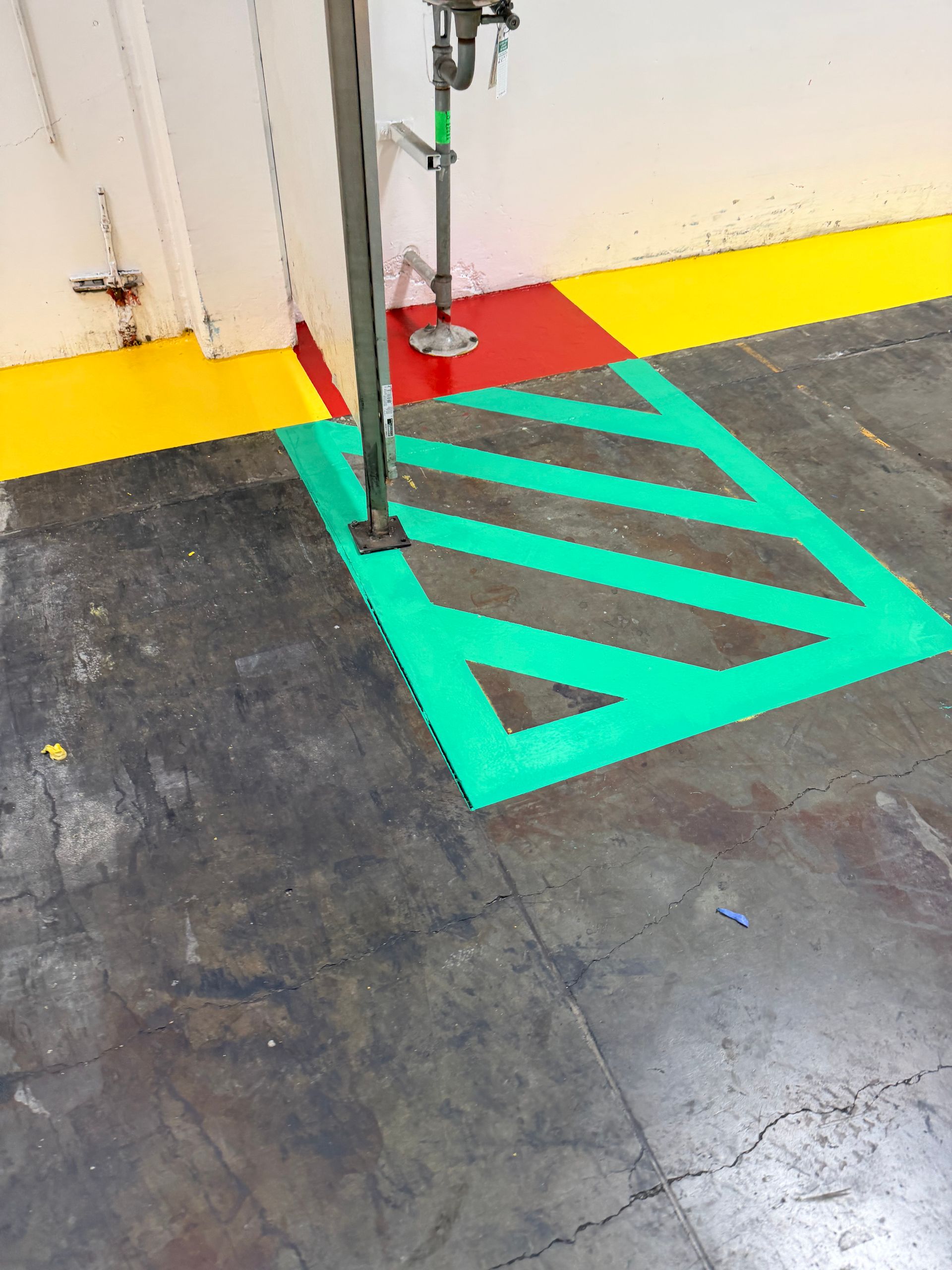 Green and red floor markings near a water pipe and metal support in a warehouse.
