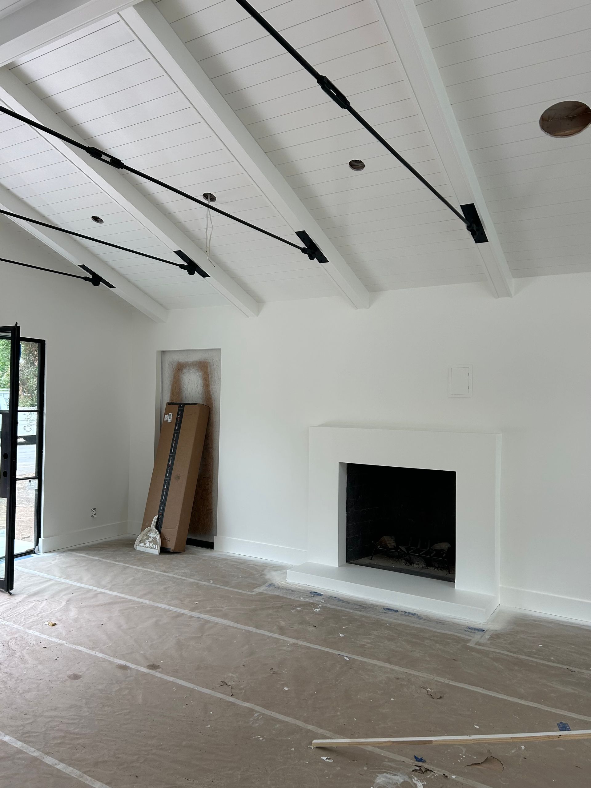 White interior room with fireplace and sloped ceiling with black beams and supports.
