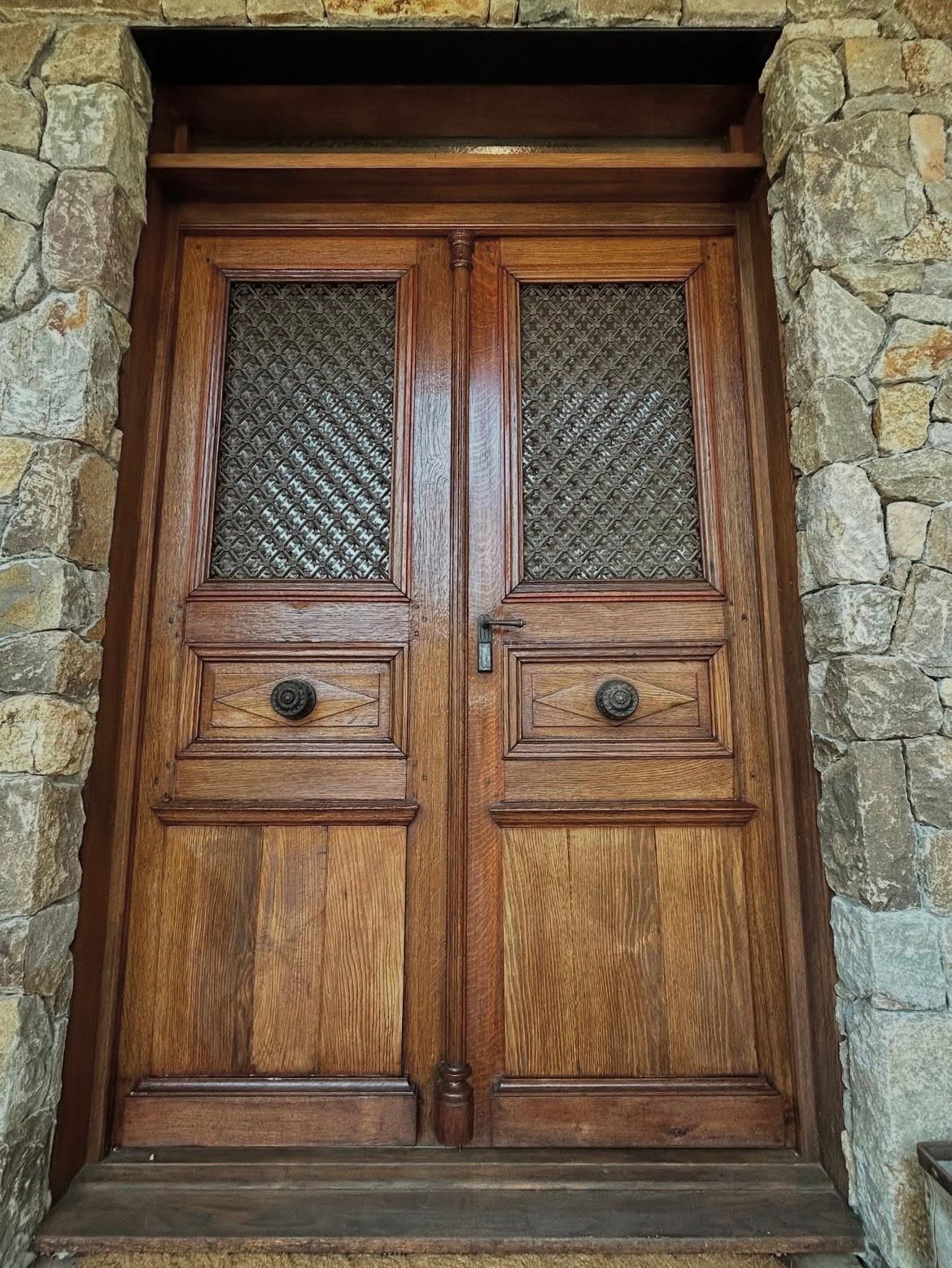 Wooden double doors with latticed glass panels, flanked by stone walls.