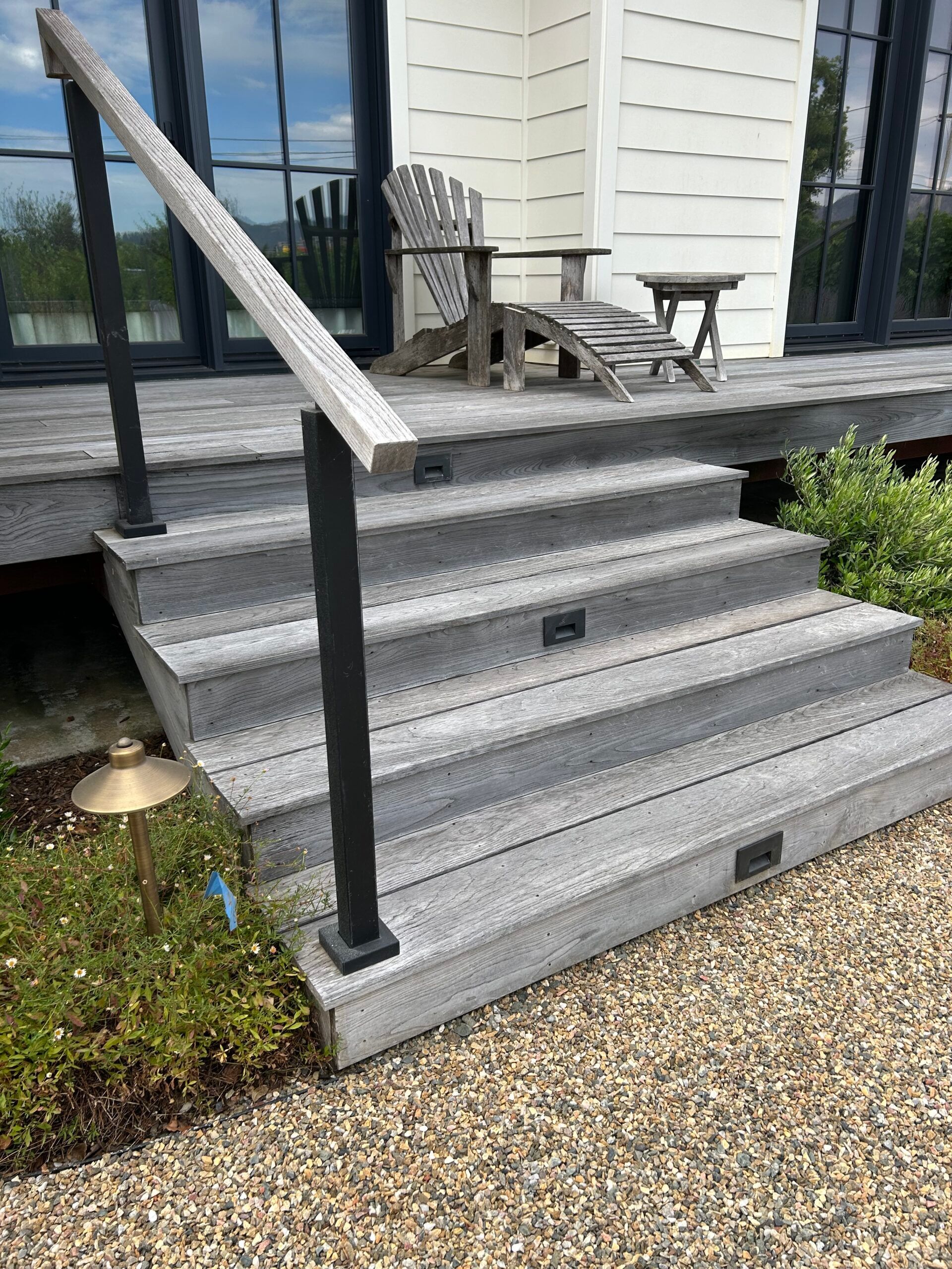 Composite gray outdoor stairs with black railing, small lights, leading to a deck with a chair.