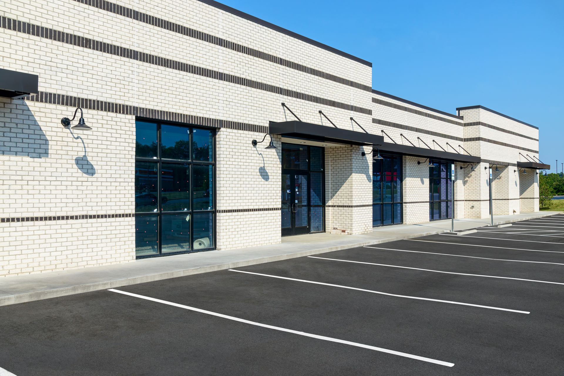 Commercial building with black awnings, windows, and parking lot. Whitewashed brick facade.