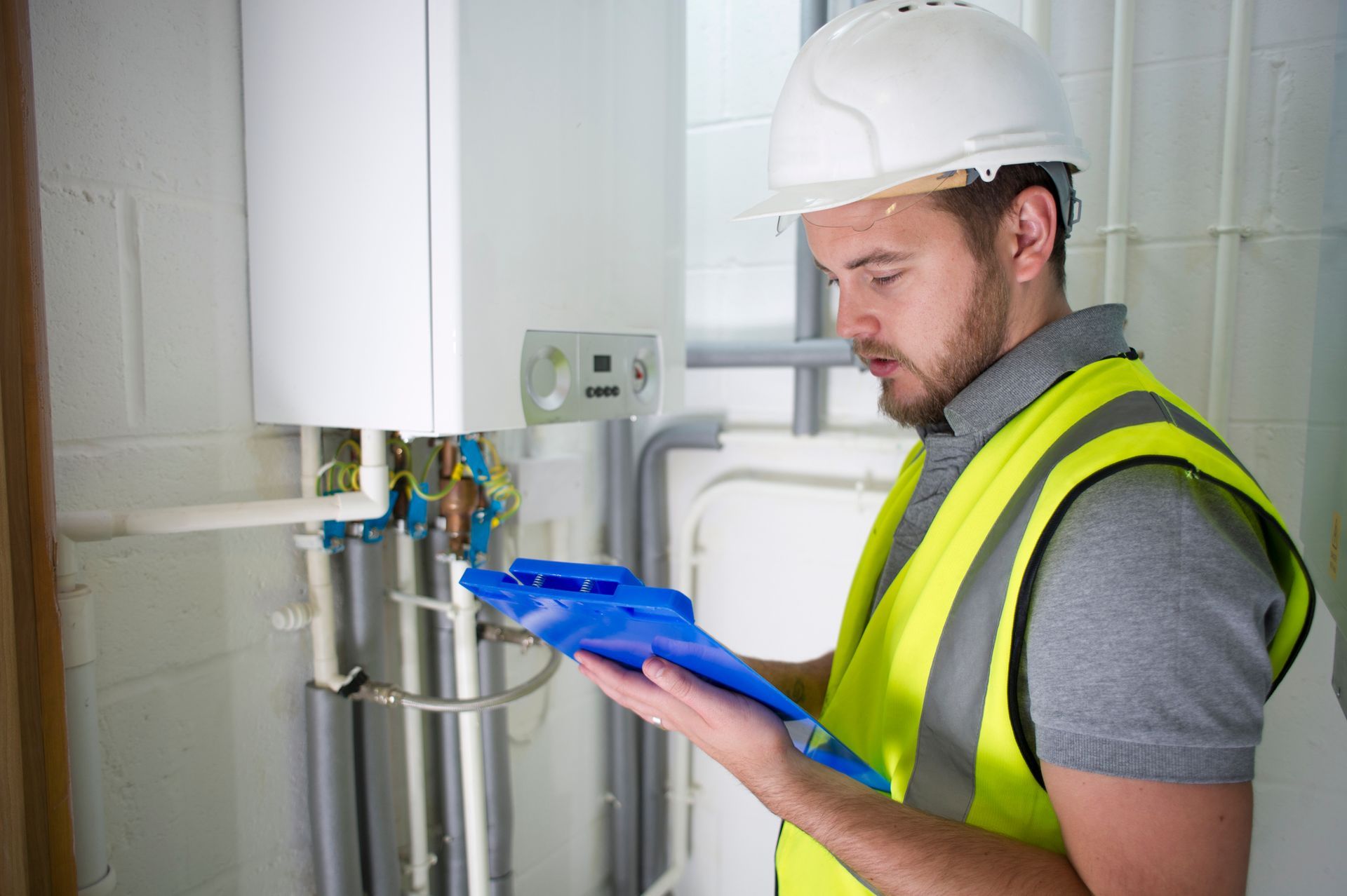Technician inspecting boiler system with clipboard during heating maintenance check.