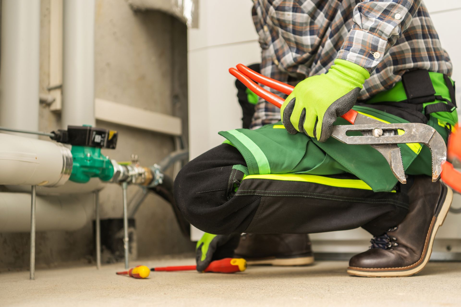 Plumber kneeling with pipe wrench fixing water pipes in utility room.