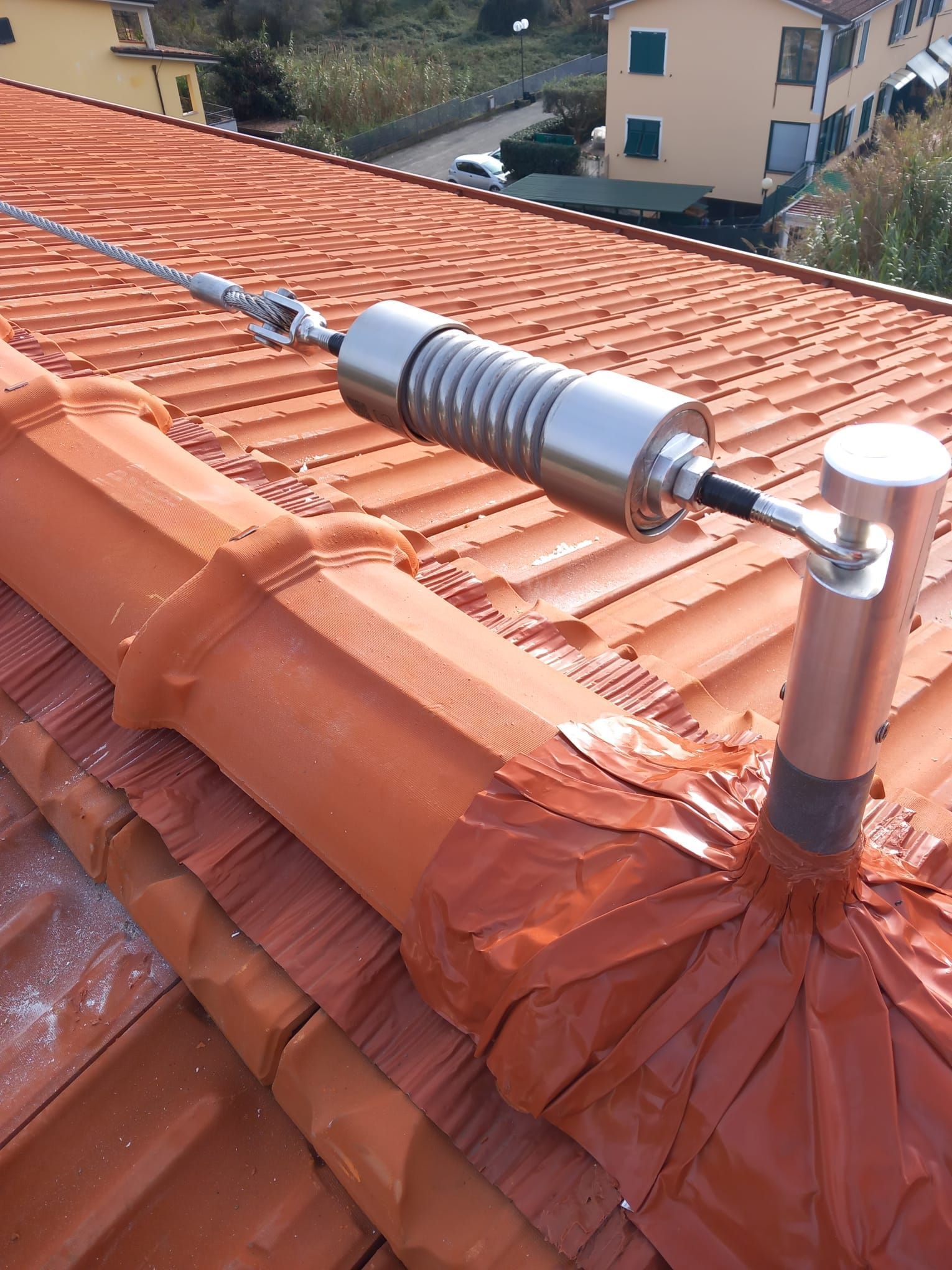 Un assorbitore di energia in acciaio inossidabile installato su una linea vita di sicurezza su un tetto di tegole in terracotta.