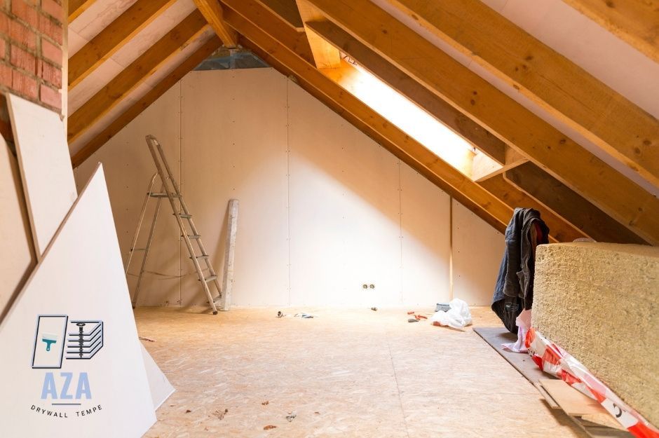 Tall, slanted attic with a window and a pile of sheetrock sheets ready for installation.