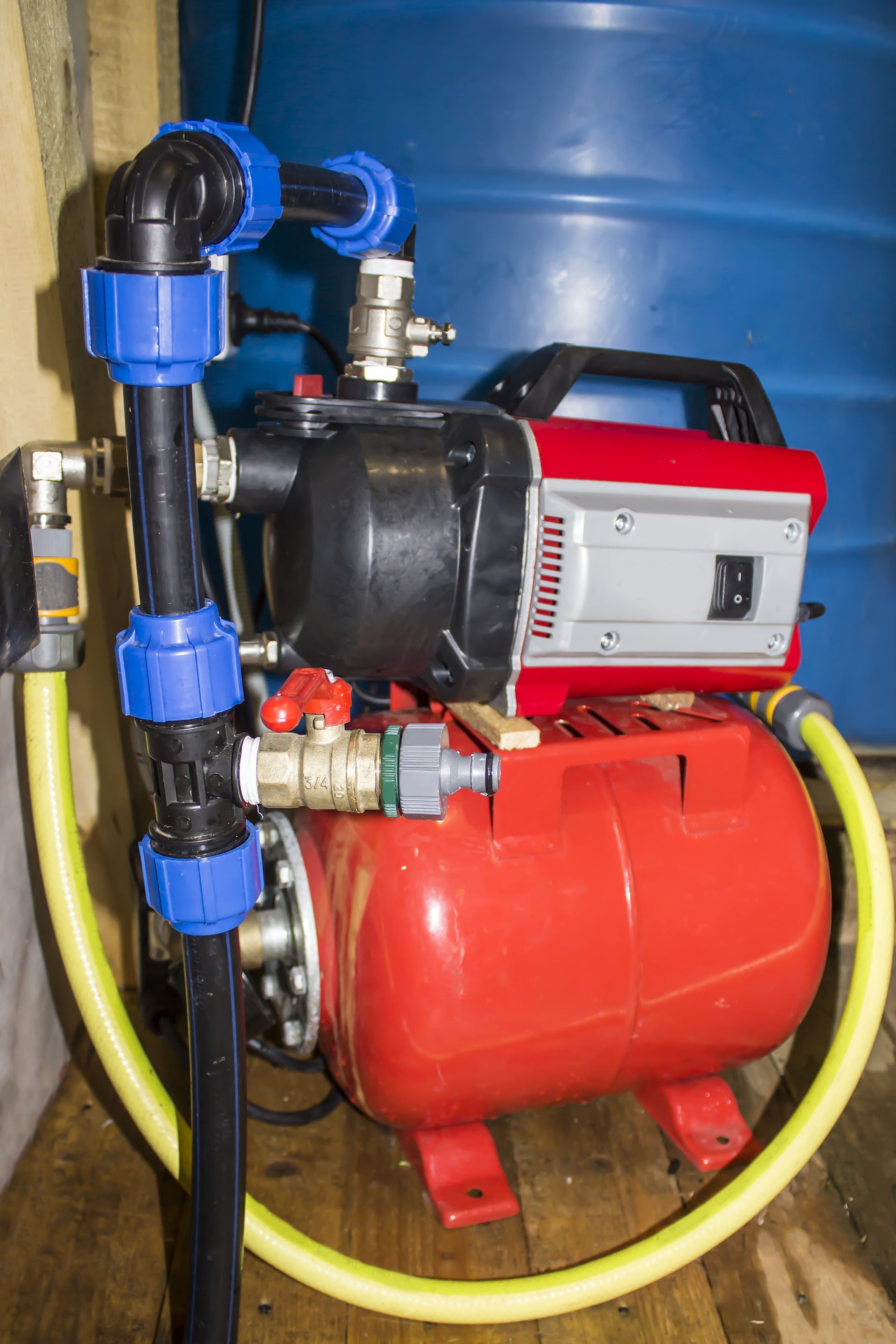 Residential water pumping station featuring pipes, hoses, and a water barrel.