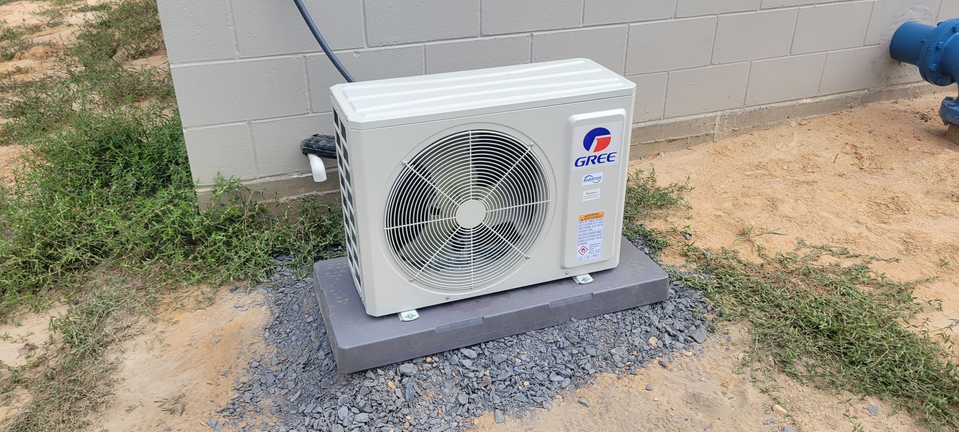 An air conditioning unit on a concrete base, set on gravel and dirt, next to a building.