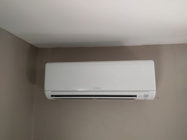 White wall-mounted air conditioning unit on a beige wall in a corner of a room.