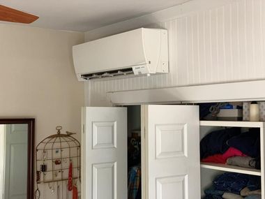 White air conditioning unit mounted on a white paneled wall above closet doors.