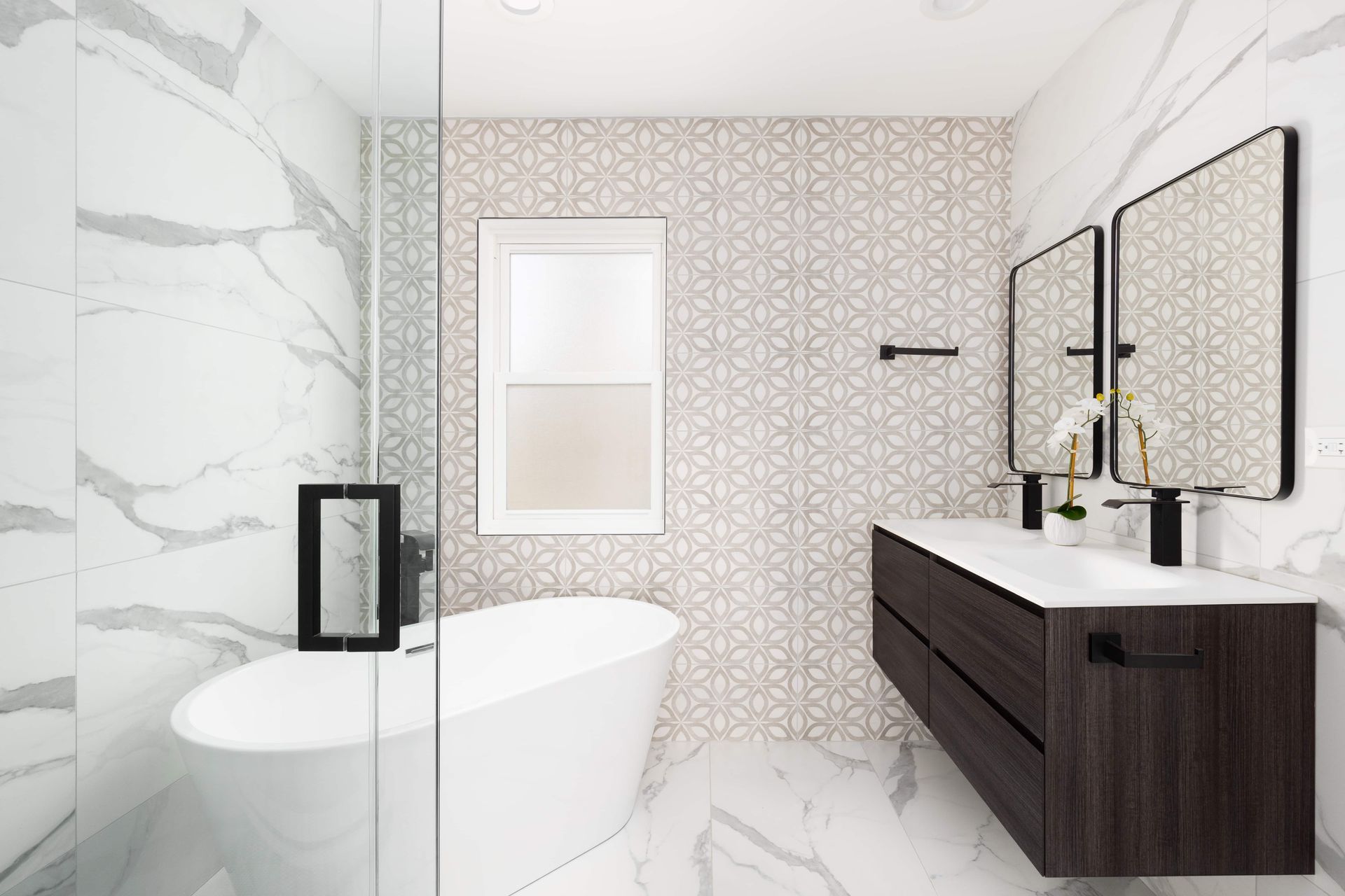 Modern bathroom with white marble and patterned tile, featuring a bathtub, double vanity, and two mirrors.