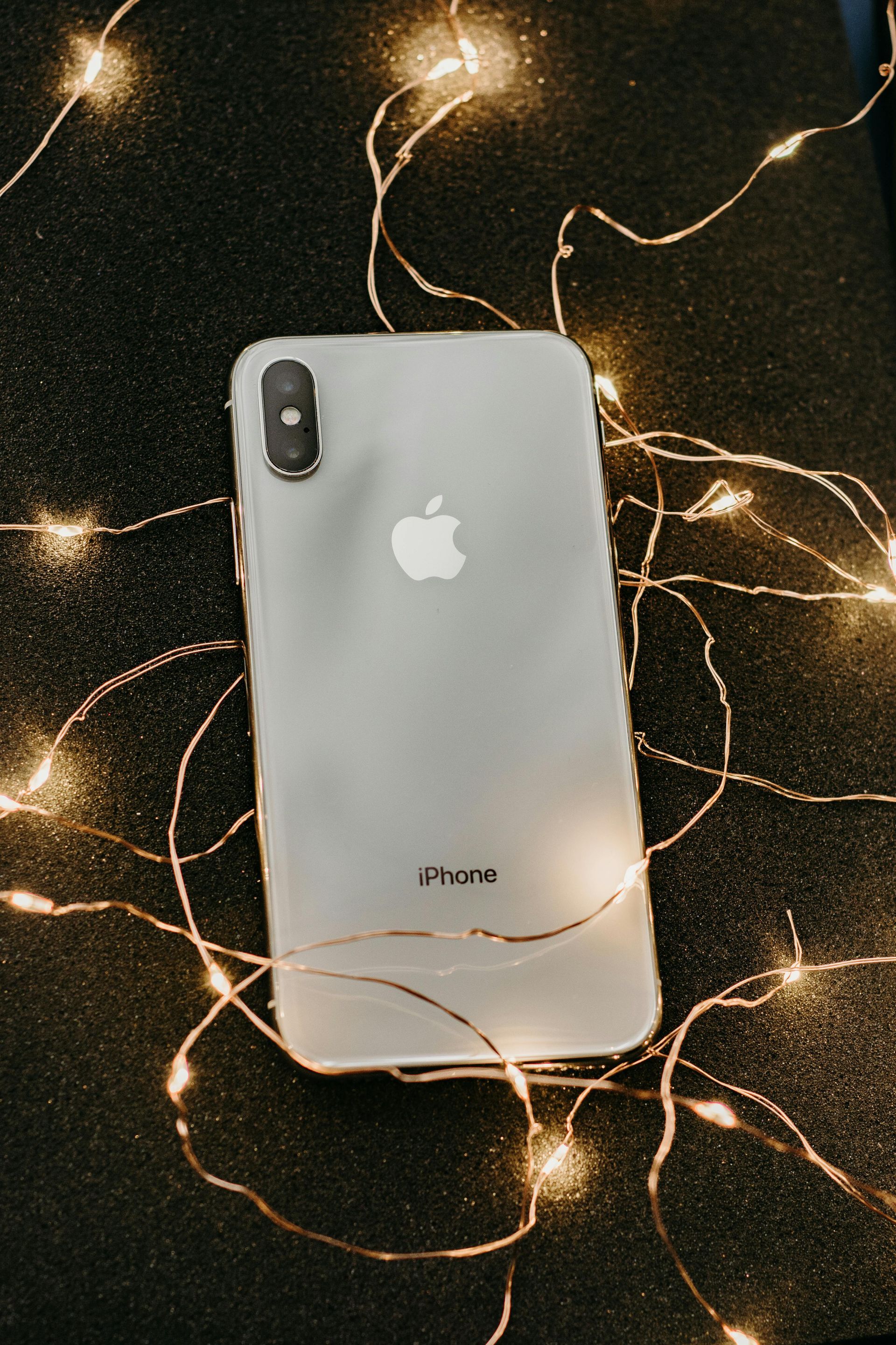 IPhone X transparente sobre una superficie negra, rodeado de luces de colores brillantes.