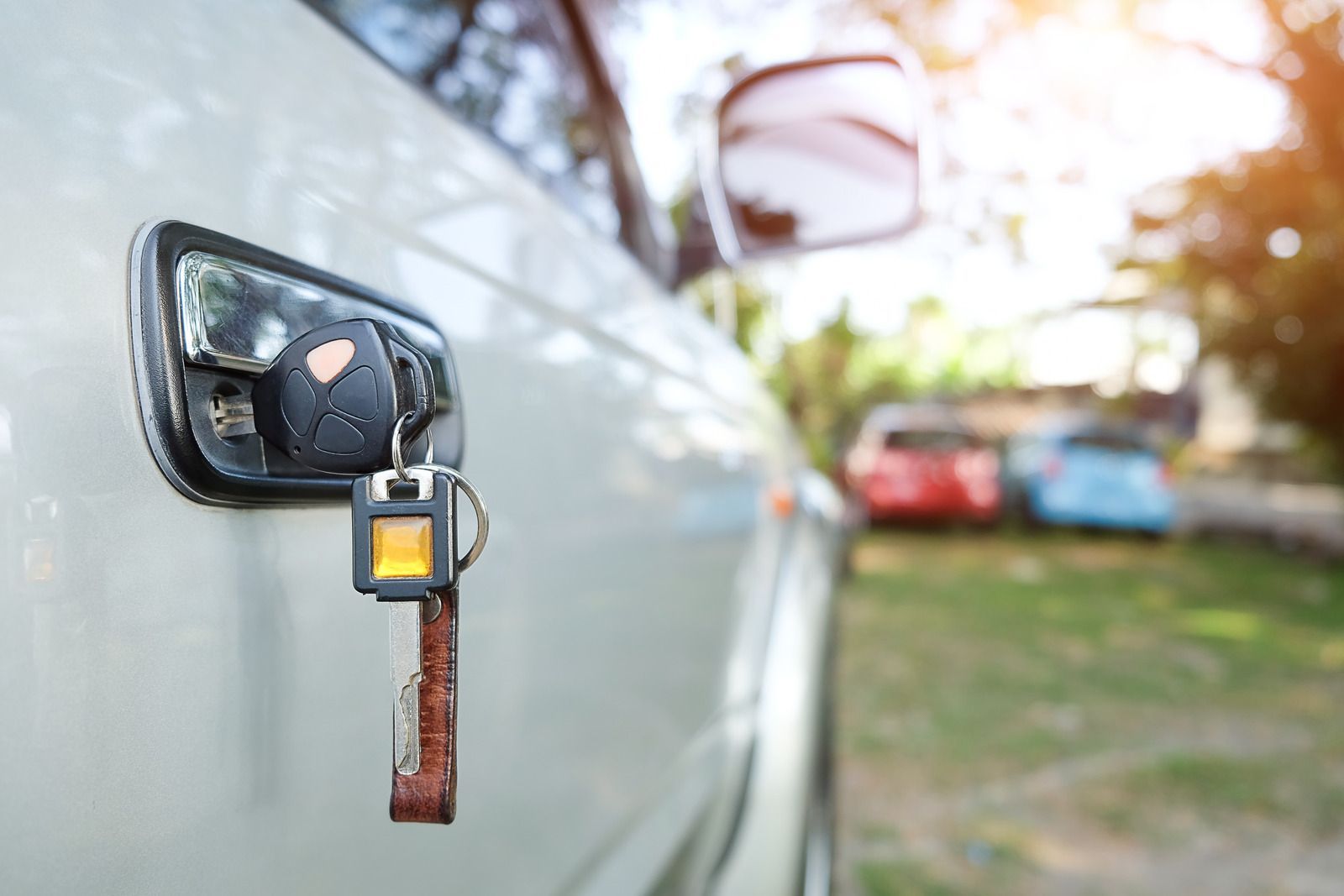 Car key hanging from a car door handle; a red and blue car in the background.