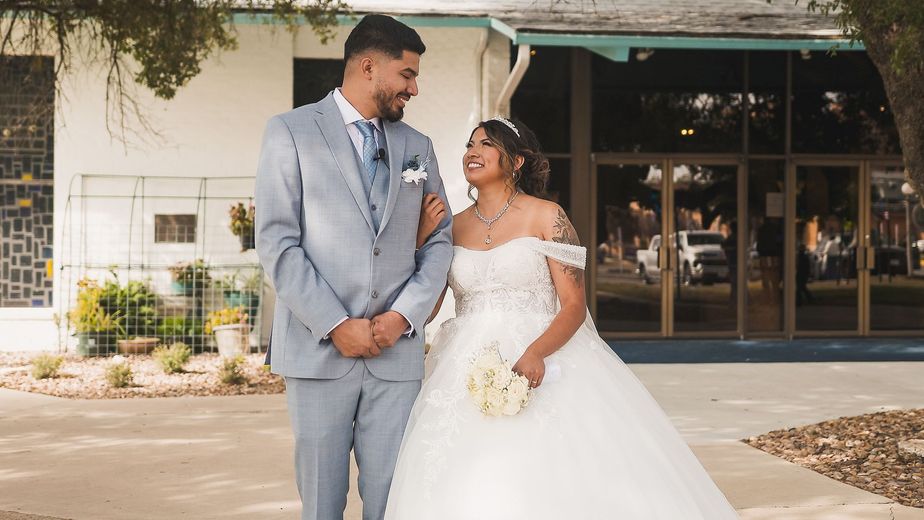 A bride and groom are posing for a picture in front of a building.