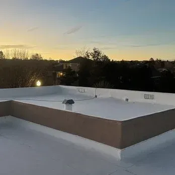 White flat roof with tan trim; trees and buildings in the background at sunset.