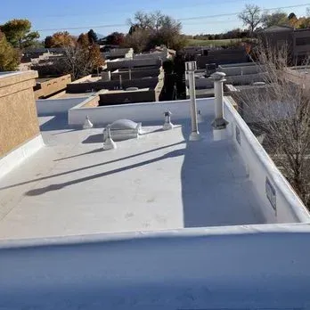 Flat white roof with vents and parapet walls under a blue sky.