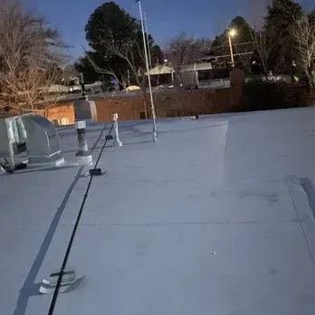 Rooftop with HVAC units and safety cables. Dusk setting with trees and buildings in the background.