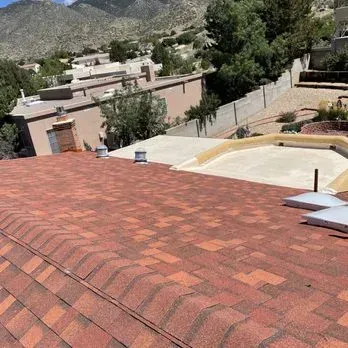 Red-shingled roof in a residential area, with a flat roof and mountain backdrop.