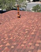 Red and brown asphalt shingle roof with a chimney, outdoors on a sunny day.