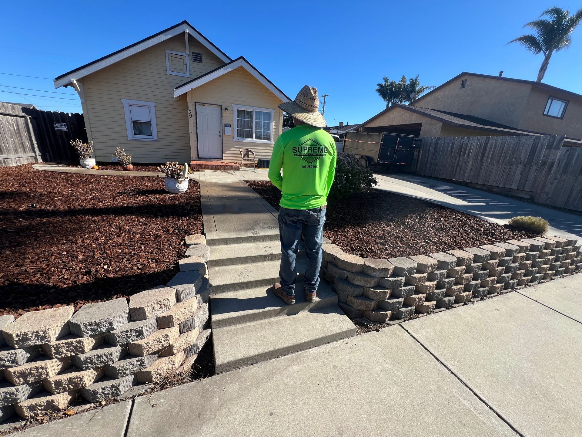 Person mowing a bright green lawn with a green and blue lawnmower; long shadow.
