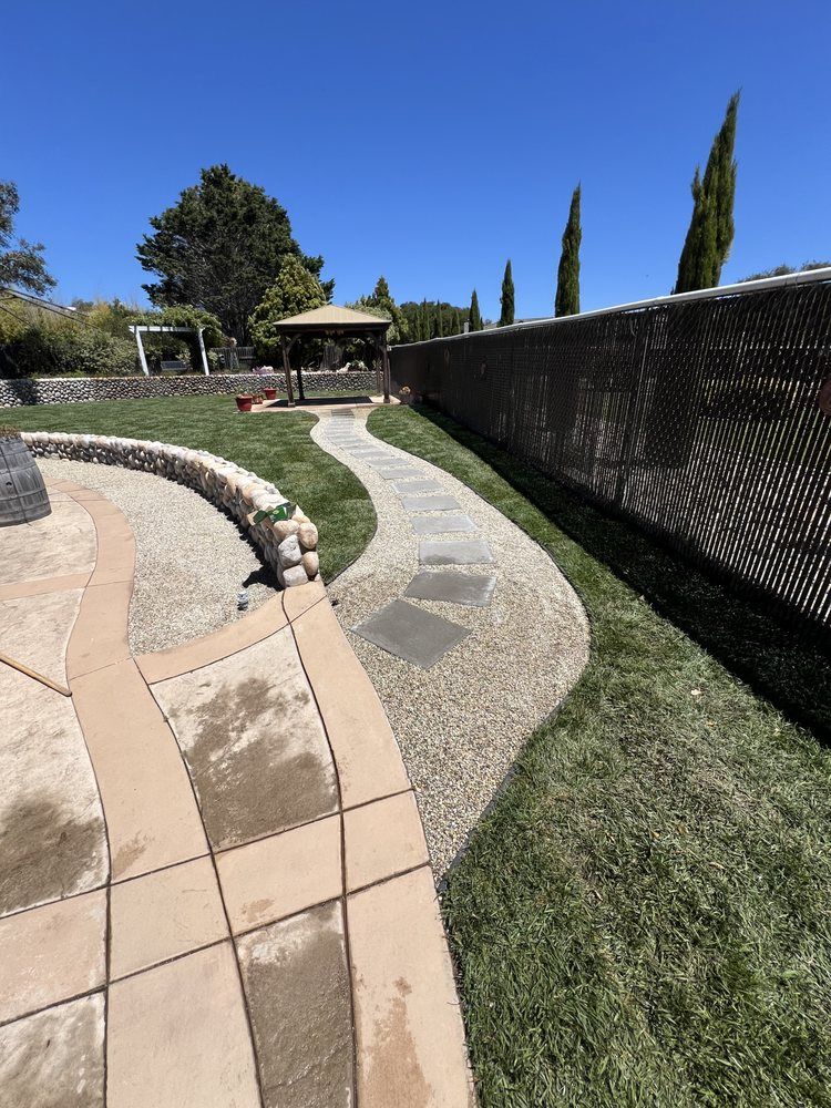 Stone pathway through a grassy backyard with a gazebo, under a clear blue sky.