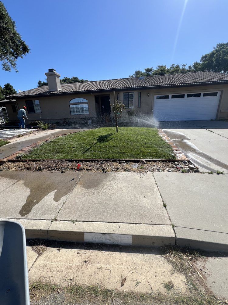 House with fresh grass being watered on a sunny day. A person is visible in the distance.