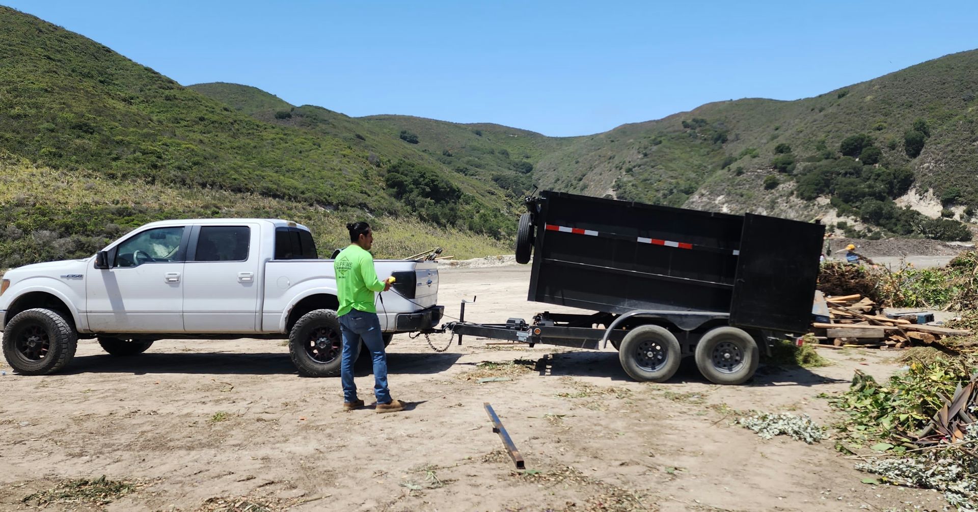 White truck with a trailer and a person standing next to them in a rural landscape.