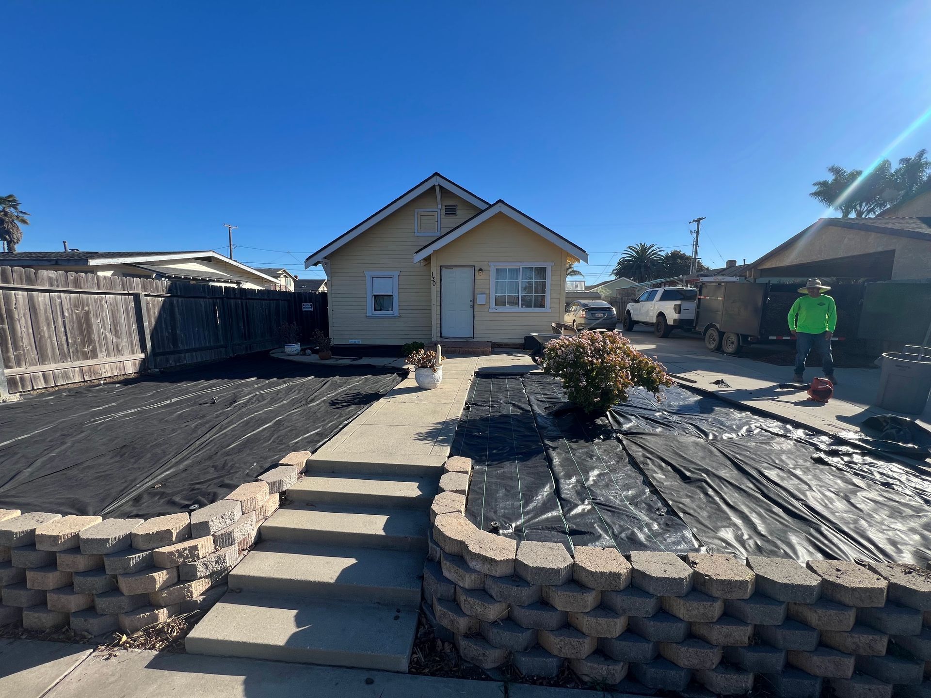 Small yellow house with a landscaped yard, raised beds, and a concrete path.