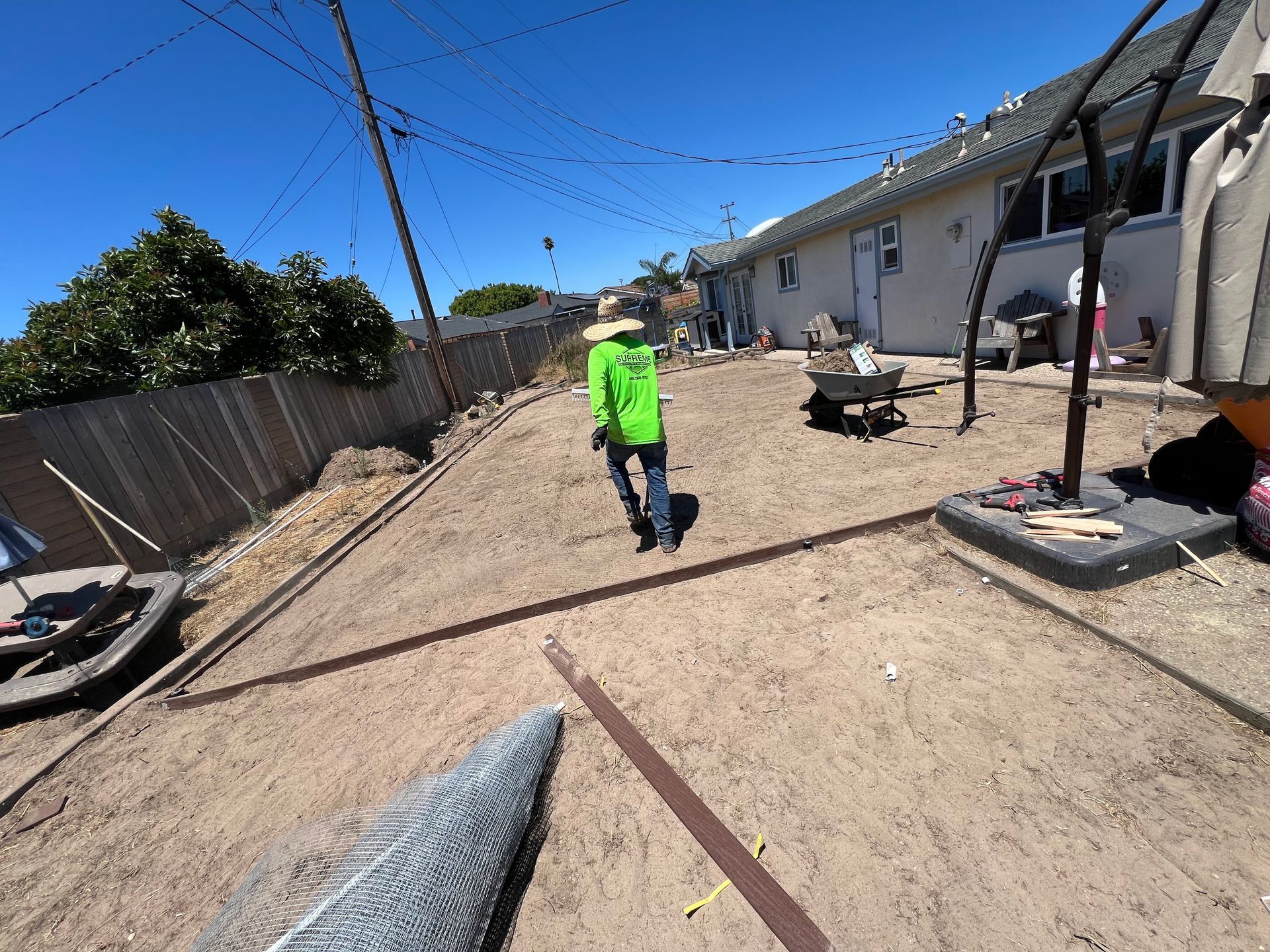 Person in neon green shirt walking in a backyard with dirt, fencing, and a house.