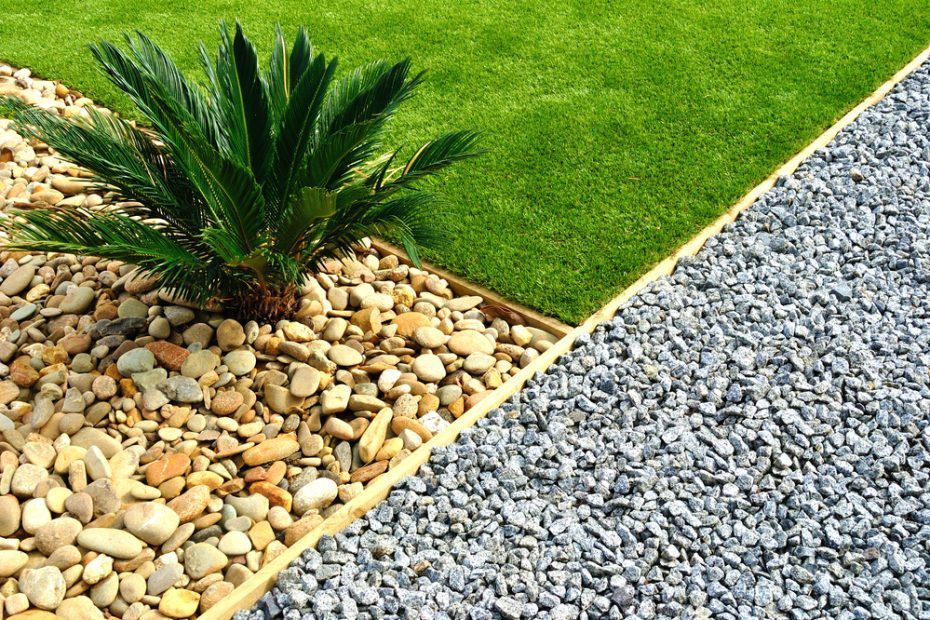 Palm plant in gravel bed bordered by artificial turf and gray gravel.