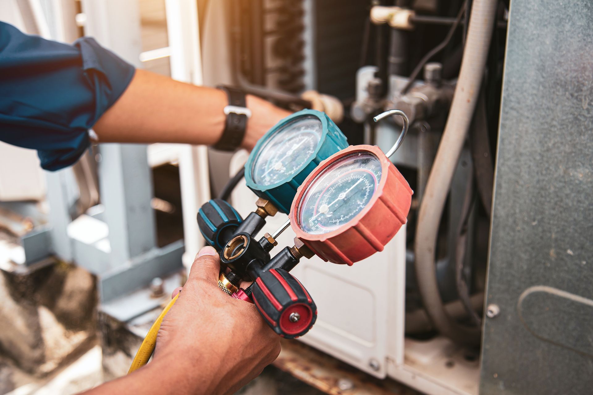 A man is working on an air conditioner with a pair of gauges.