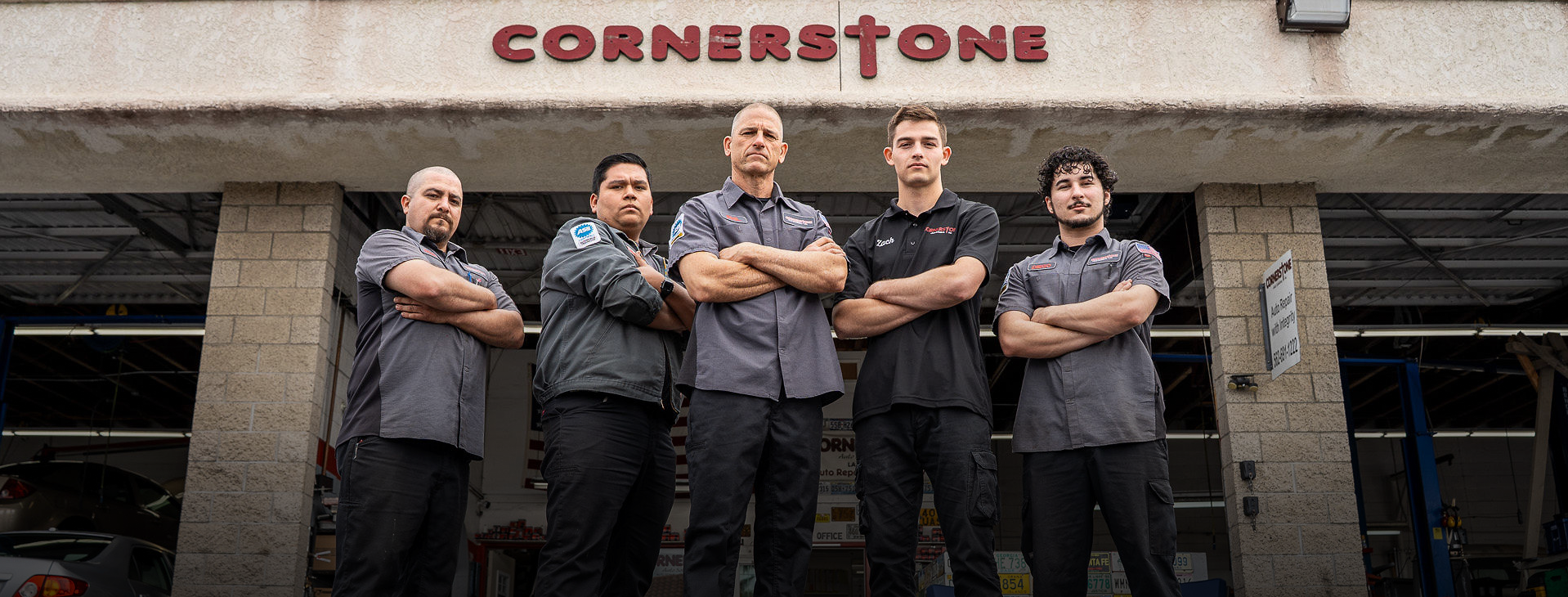 Five people stand with arms crossed in front of a building with a sign that reads