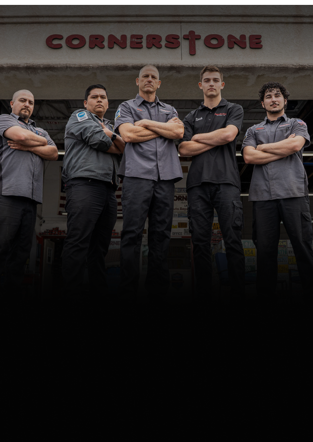 Five people in grey uniforms stand with arms crossed in front of a building with a