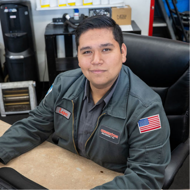 A person wearing a grey uniform jacket with a US flag patch sitting at a desk in an office. | Cornerstone Auto Solutions