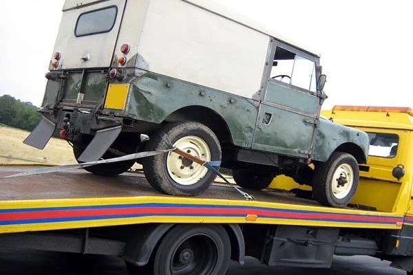 A green truck is being towed by a yellow tow truck