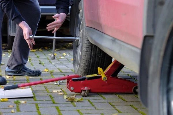 A man is changing a tire on a red car with a jack.
