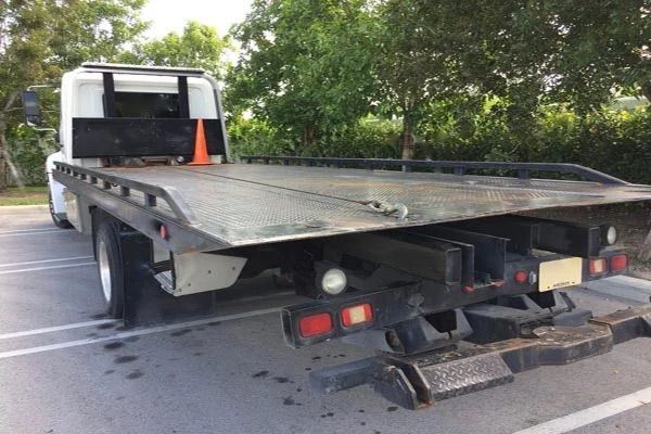 A tow truck with a flat bed is parked in a parking lot.